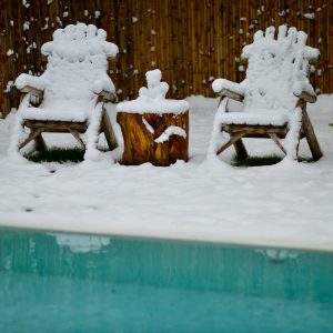 Two wooden chairs outside by the pool in the snow.  