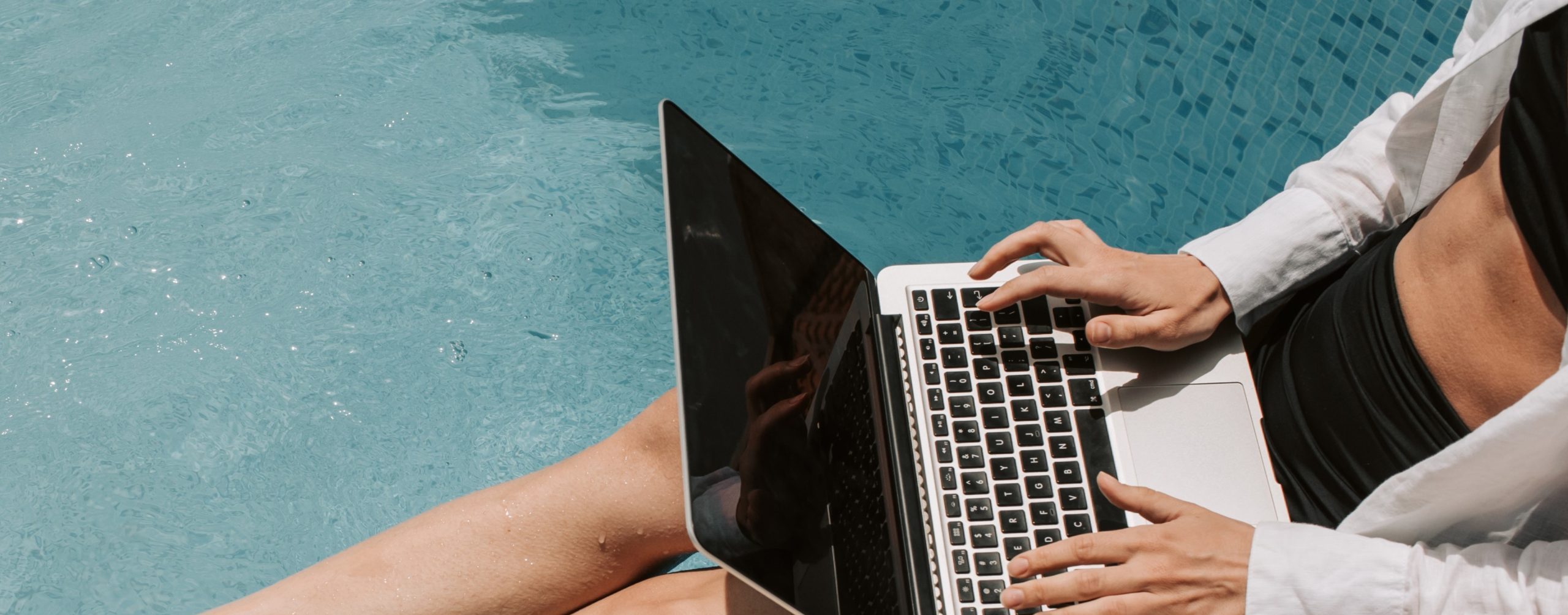 Woman sitting my the pool with a laptop.