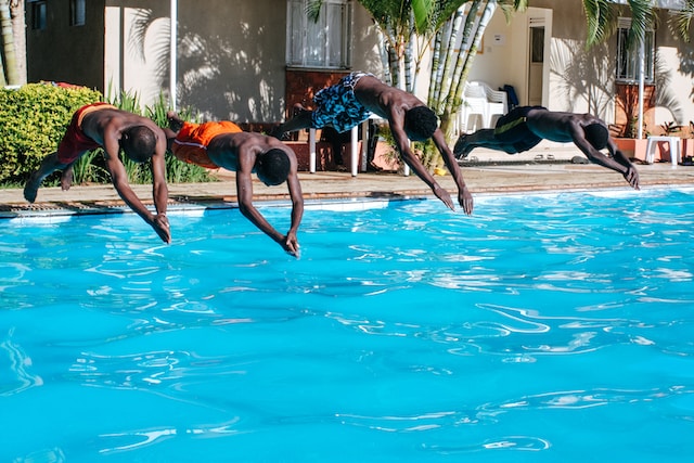 Four men jumping into a swimming pool. 