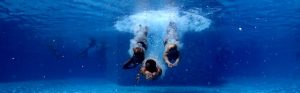 Three people swimming underwater in a pool.