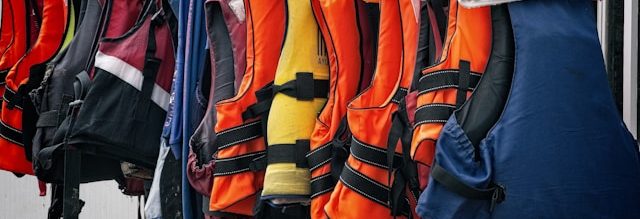 A bunch of life jackets hanging on a clothes rack.