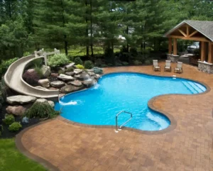 Backyard swimming pool with a curved water slide, brick patio, lounge chairs, and a covered seating area, surrounded by trees and landscaping.